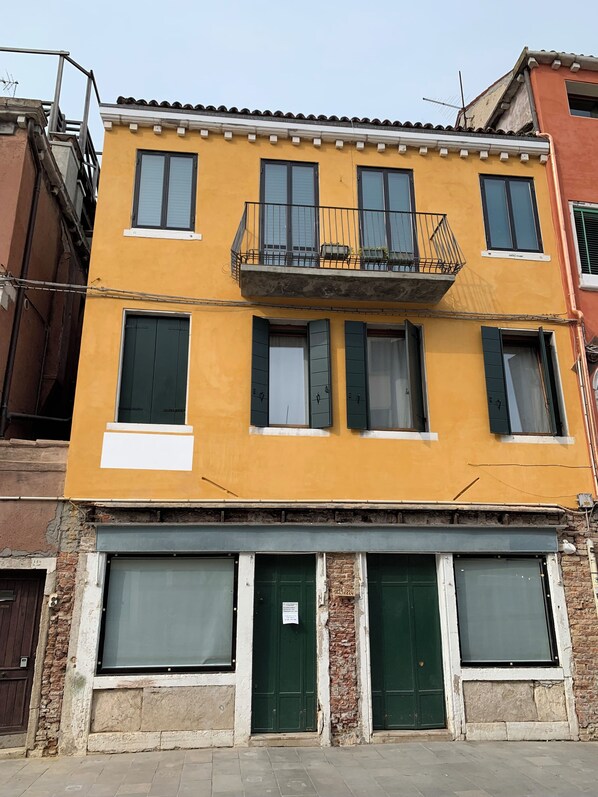 A yellow building with a balcony, multiple windows, and a brick facade.