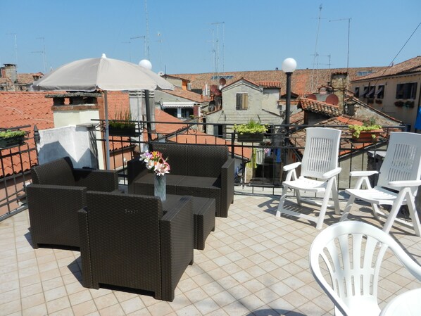 A rooftop terrace with wicker furniture, a potted plant, and a white umbrella.