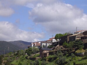 A hillside village with traditional stone buildings, a small wooden structure, and a view of the surrounding hills.