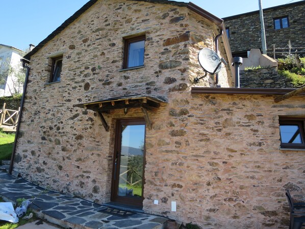A stone building with a wooden door, a satellite dish, and a small window.
