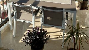 Een balkon met een tafel en stoelen, potplanten en uitzicht op zee en bergen.