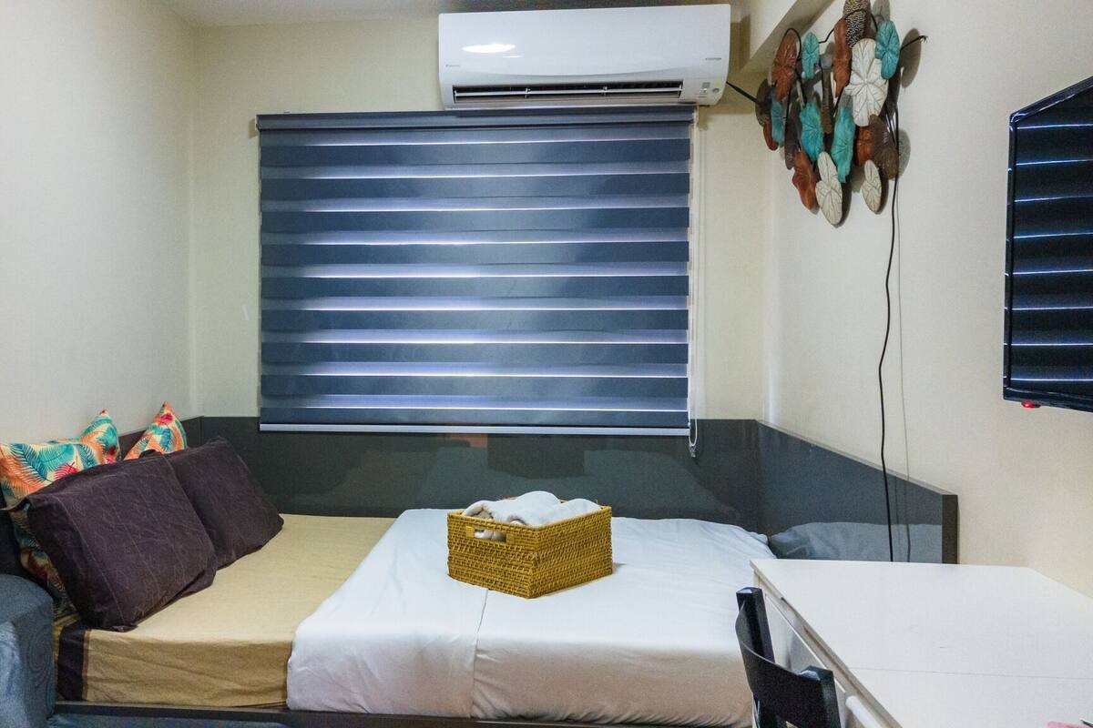 A small, compact room with a bed, a desk, and a window with blinds.