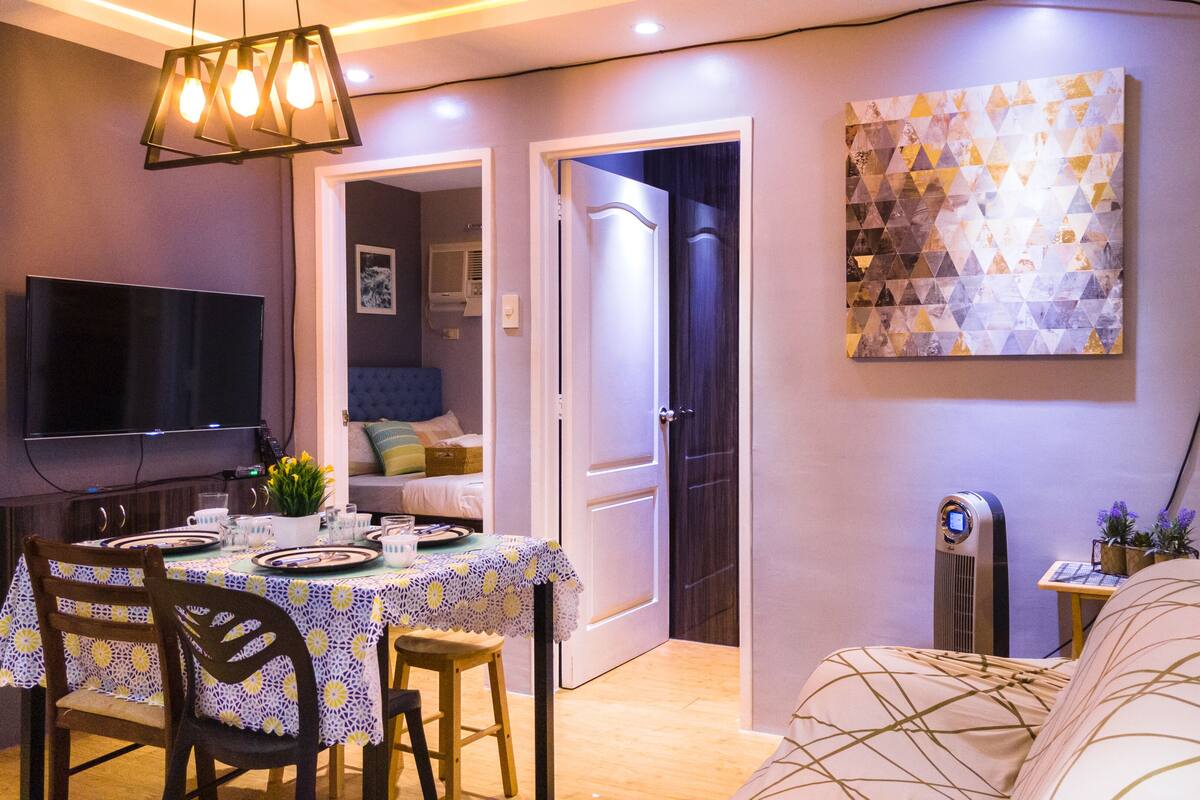 A modern living room with a dining area, a flat-screen TV, and a decorative wall piece.