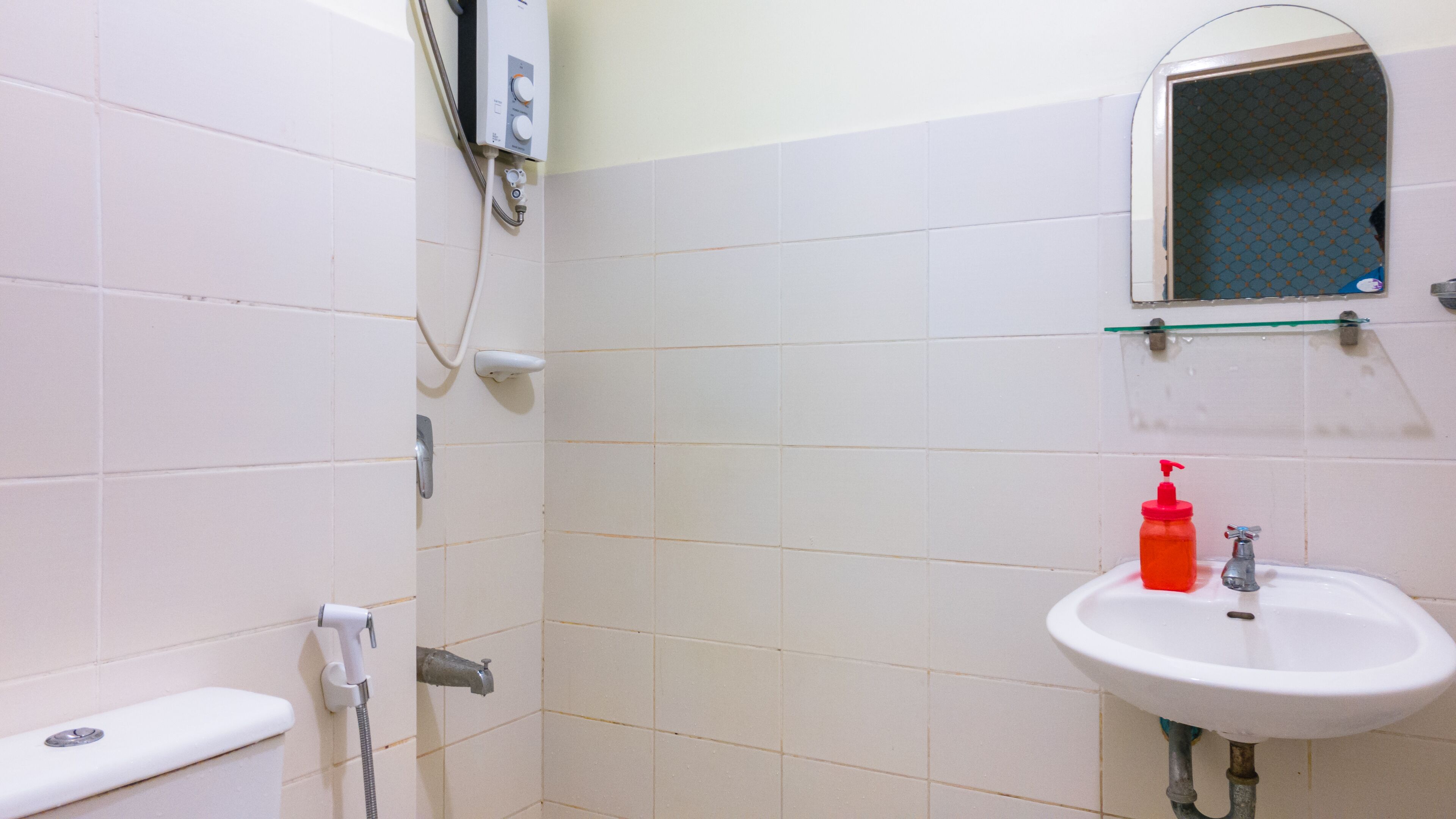 Une salle de bain avec des carreaux blancs, des toilettes, un lavabo et une douche.