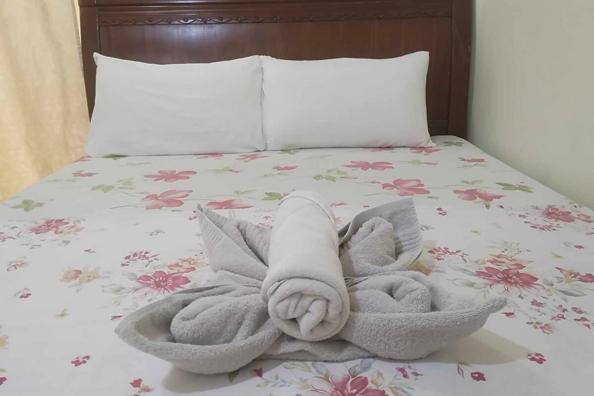 A neatly made bed with floral bedding and a towel arranged in a flower shape.