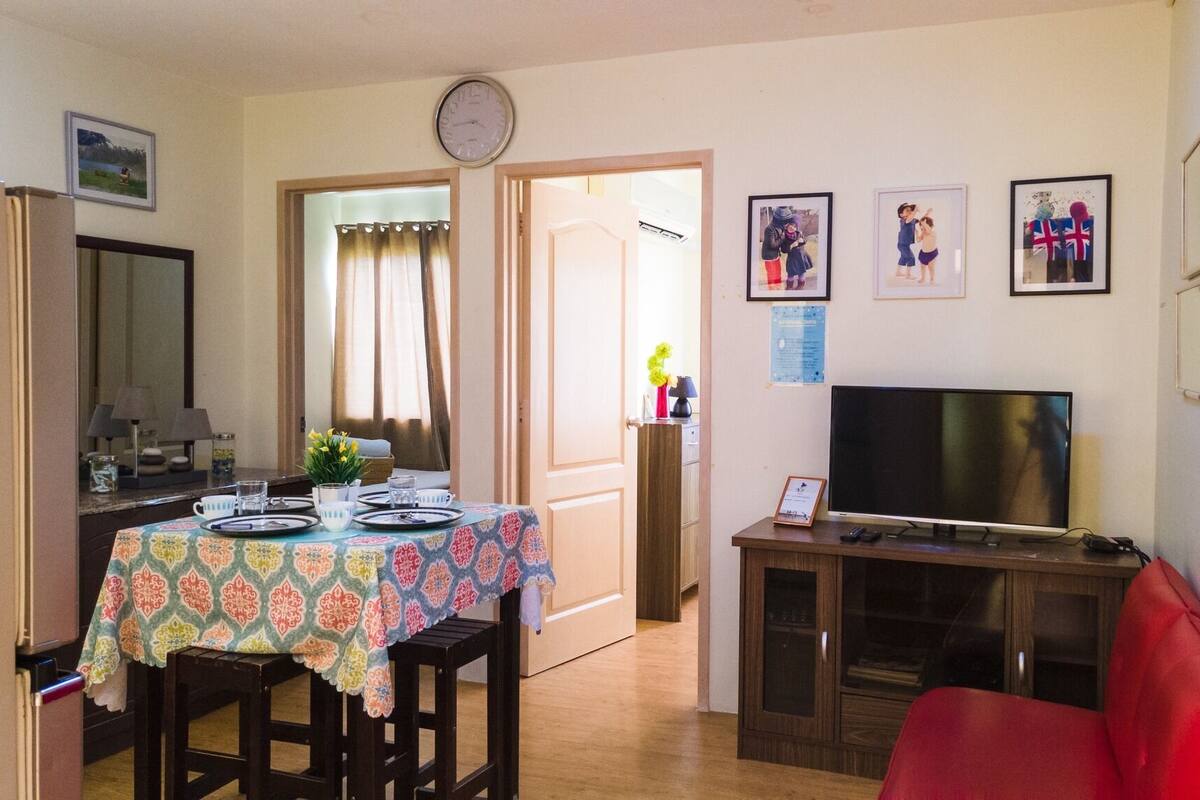 A dining area with a table set for four, a television on a cabinet, and a red chair.