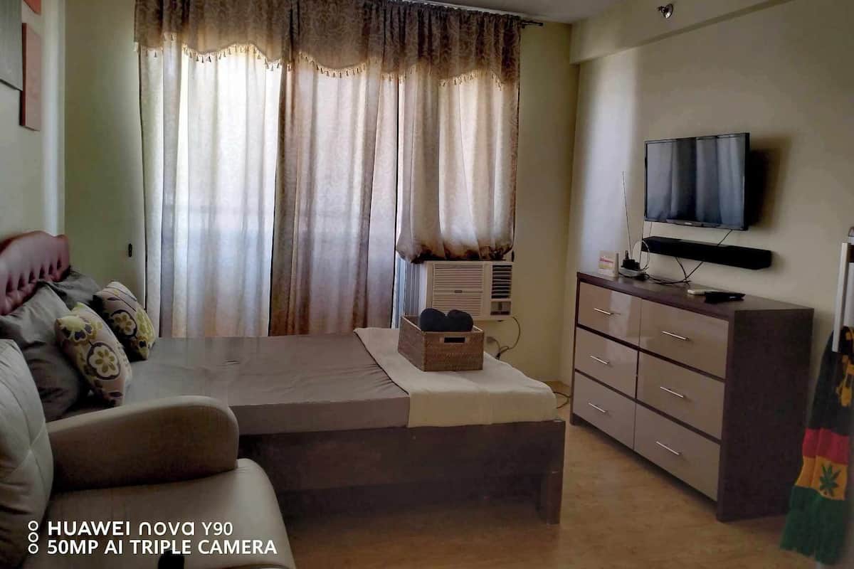 A hotel room with a bed, a sofa, a TV, a dresser, and a window with curtains.