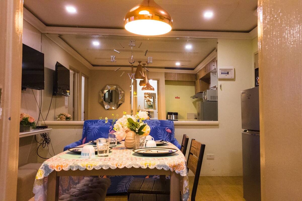 A dining area with a table set for two, a decorative vase, and a ceiling light fixture.