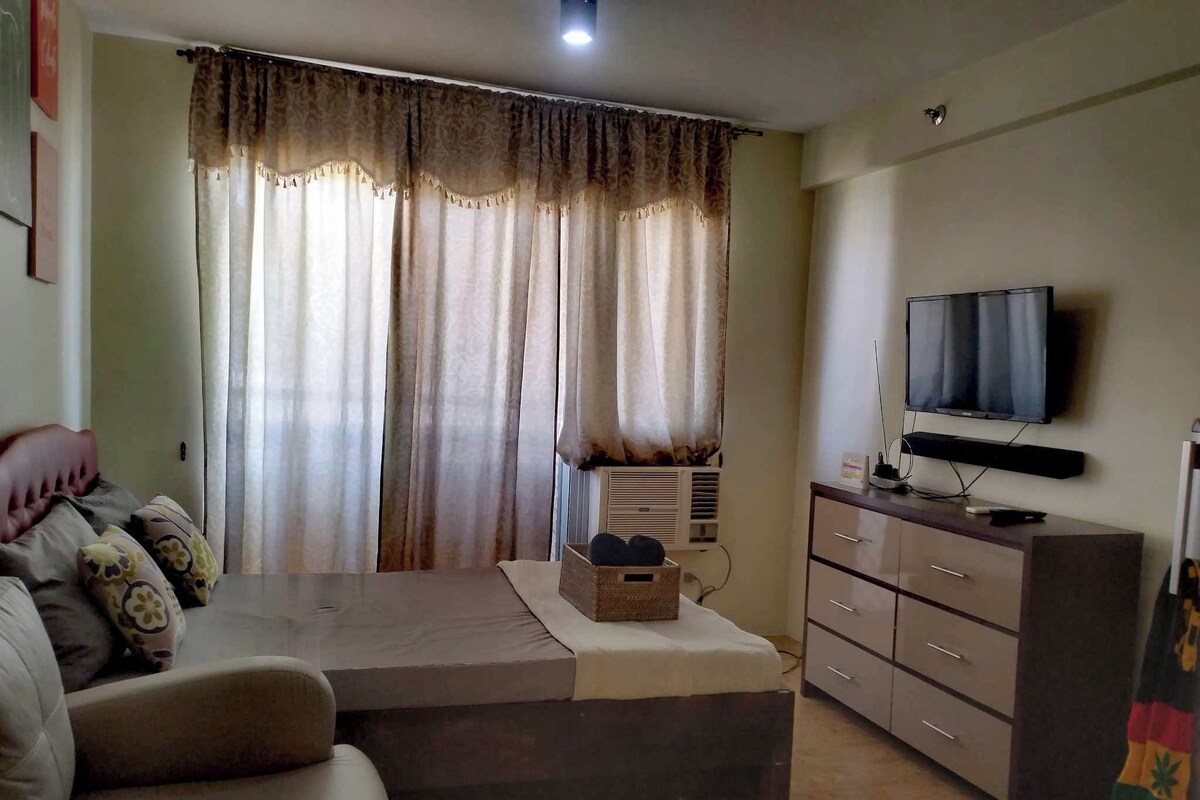 A hotel room with a bed, a sofa, a TV, a dresser, and a window with curtains.