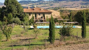 Una villa de piedra con piscina, rodeada de árboles y colinas.
