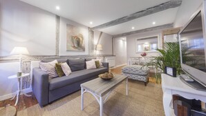 Een moderne woonkamer met een grijze bank, een houten salontafel, een televisie en een kamerplant.