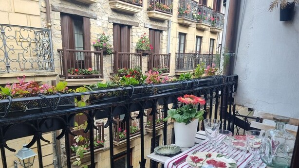 Een balkon met een eettafel, plantenbakken en uitzicht op omliggende gebouwen.