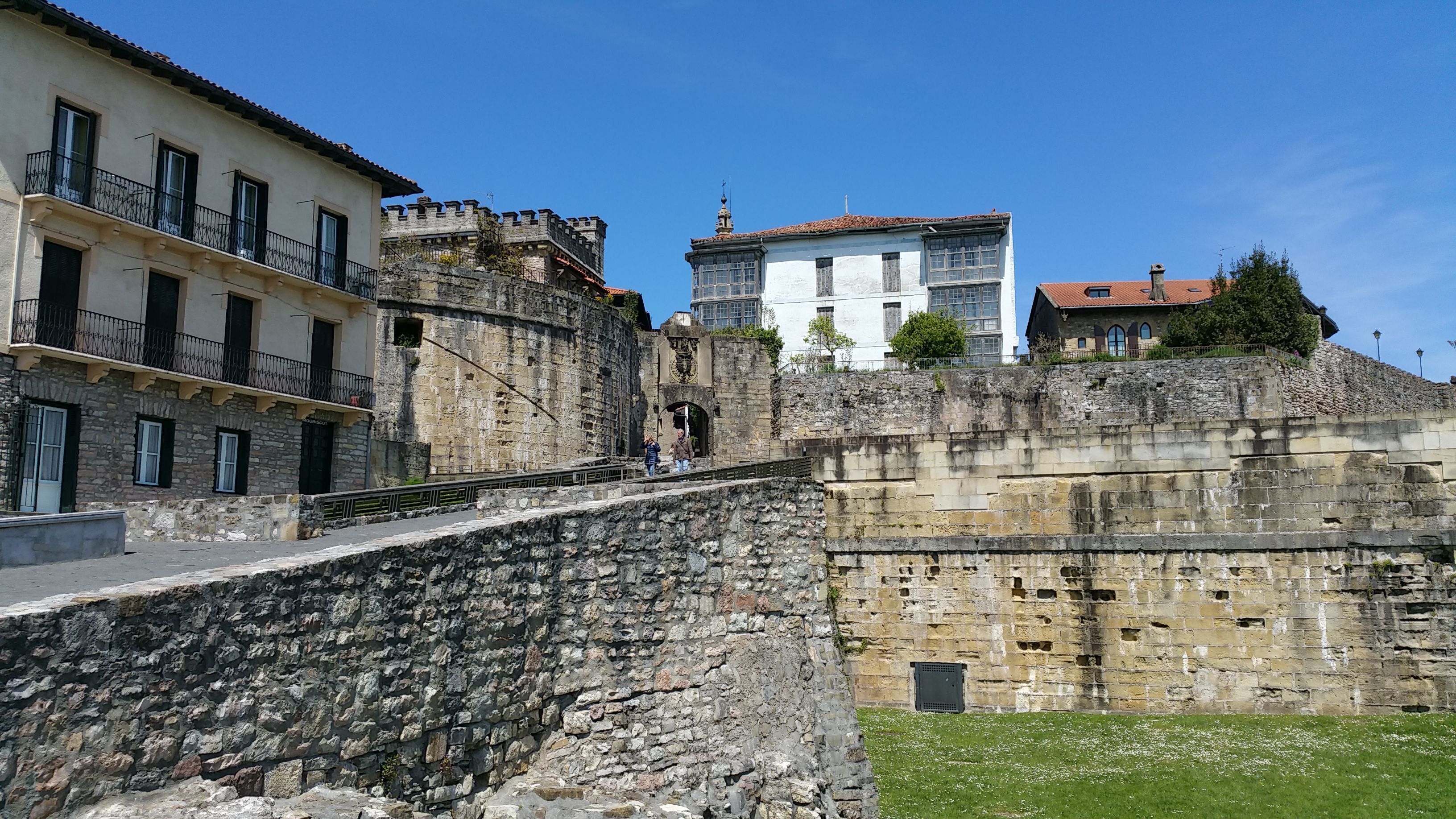 A stone wall with a staircase leading to a building with a white facade and a red roof.