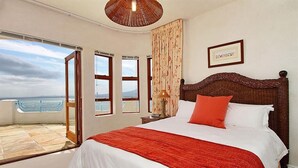 A bedroom with a large bed, a view of the sea through a sliding door, and a framed picture on the wall. - Private villa in Gordons Bay with ocean views and pool (Cape Town)