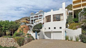 A modern white building with a garage, a balcony, and a staircase leading to a second floor. - Private villa in Gordons Bay with ocean views and pool (Cape Town)