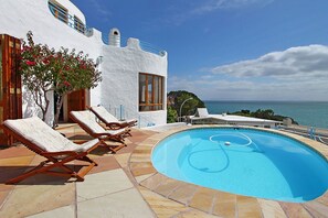 A pool area with lounge chairs, a clear blue pool, and a view of the sea. - Private villa in Gordons Bay with ocean views and pool (Cape Town)
