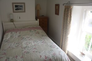 A bedroom with a bed, a dresser, a lamp, a framed picture, and a window with curtains.