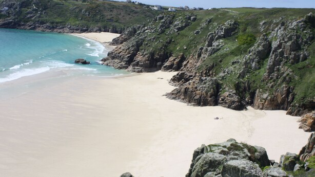 A coastal landscape with a sandy beach, rocky cliffs, and a clear view of the sea.