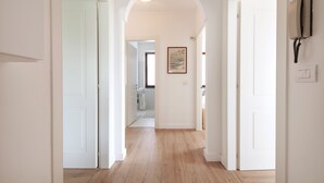 A hallway with a wooden floor, white walls, and a door leading to a bathroom.