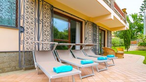 A patio with sun loungers, a garden, and a building with decorative ironwork.