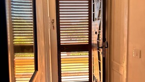 Een smalle gang met een deur naar een balkon. De gang heeft een betegelde vloer en een witte muur.