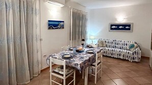 A dining area with a table set for four, a sofa, and two wall-mounted fish paintings.