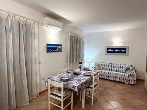 Zona pranzo con tavolo apparecchiato per quattro persone, una poltrona e due dipinti di pesci appesi al muro.