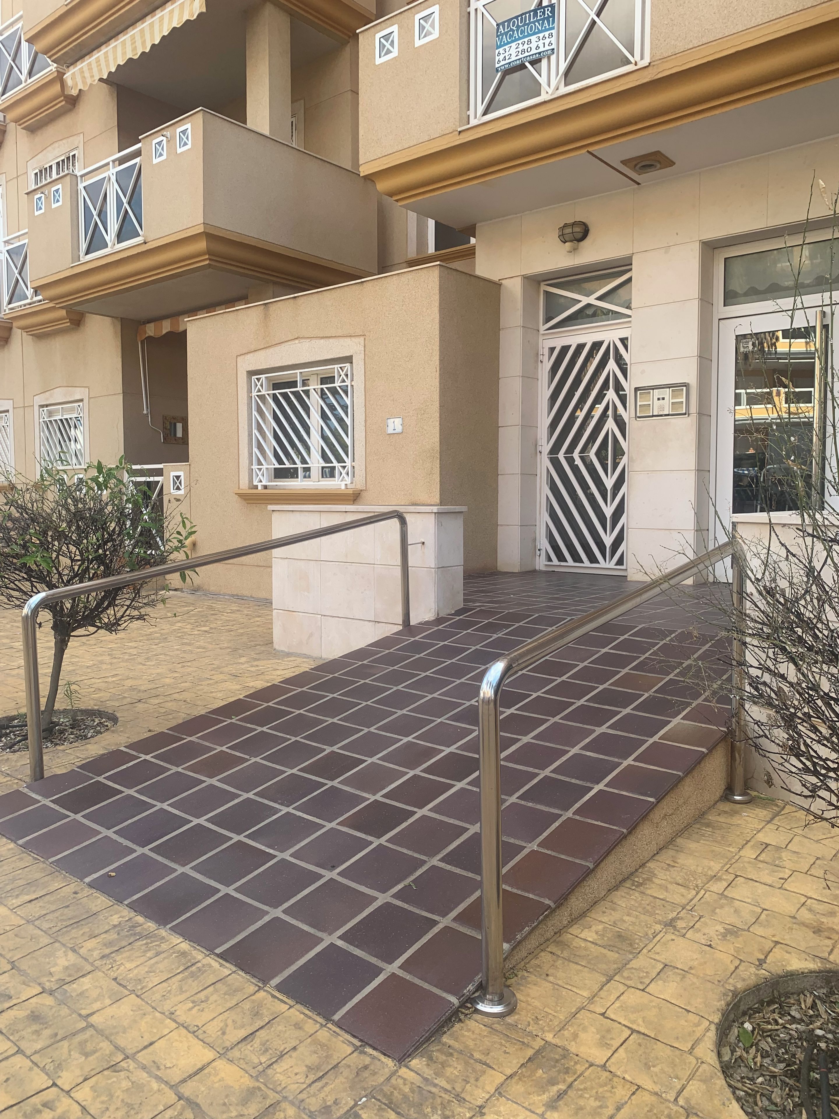 Un edificio de varios pisos con una rampa de acceso, barandales metálicos y una planta baja con azulejos.