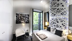 A modern hotel room with a bed, a chair, a painting, and a balcony with a view of greenery. - Ale Maison Deluxe and exclusive apartment in the best center of Seville. parking (Sevilla)