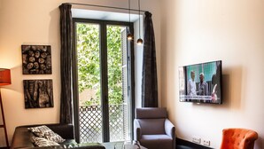 A modern living room with a dining table set for two, a sofa, a chair, and a television mounted on the wall. - Ale Maison Deluxe and exclusive apartment in the best center of Seville. parking (Sevilla)