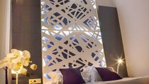 A modern hotel room with a bed, a bedside table, a lamp, and a decorative screen. - Ale Maison Deluxe and exclusive apartment in the best center of Seville. parking (Sevilla)