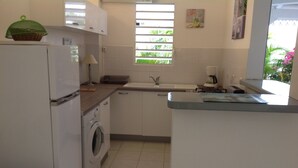 Una cocina pequeña con lavadora, un lavamanos y una ventana con persianas.