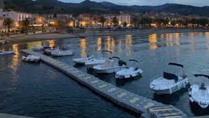 Un porto turistico con imbarcazioni ormeggiate, una passeggiata lungomare e edifici sullo sfondo.