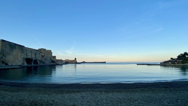 Paesaggio costiero con una struttura fortificata, acque calme e cielo sereno.