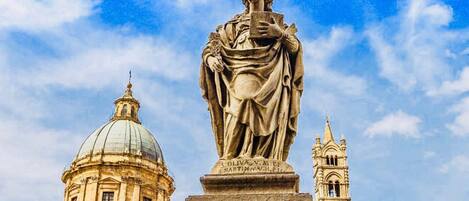 Una estatua de una mujer sosteniendo un libro, con una cúpula y un campanario al fondo.