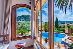 A room with a large window overlooking a swimming pool and a mountainous landscape. - Can Simone - House in old town pollensa few steps to center and nice views (Pollença)