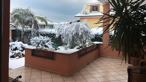 Un balcone con piante innevate e vista su un edificio giallo.