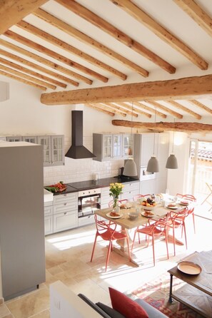 A modern kitchen with wooden beams, white cabinets, and a dining area with red chairs.