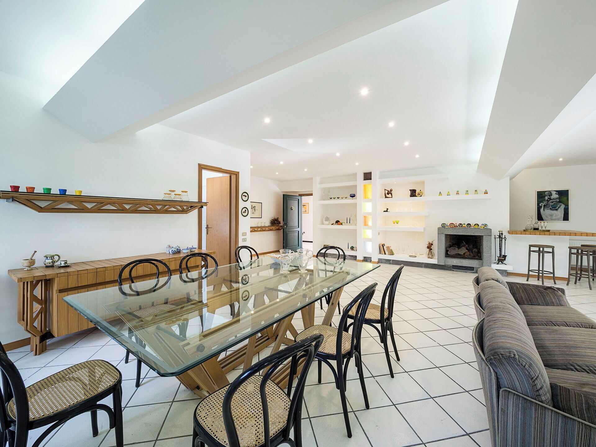 A spacious living area with a glass-top dining table surrounded by chairs, a sofa, and a fireplace.