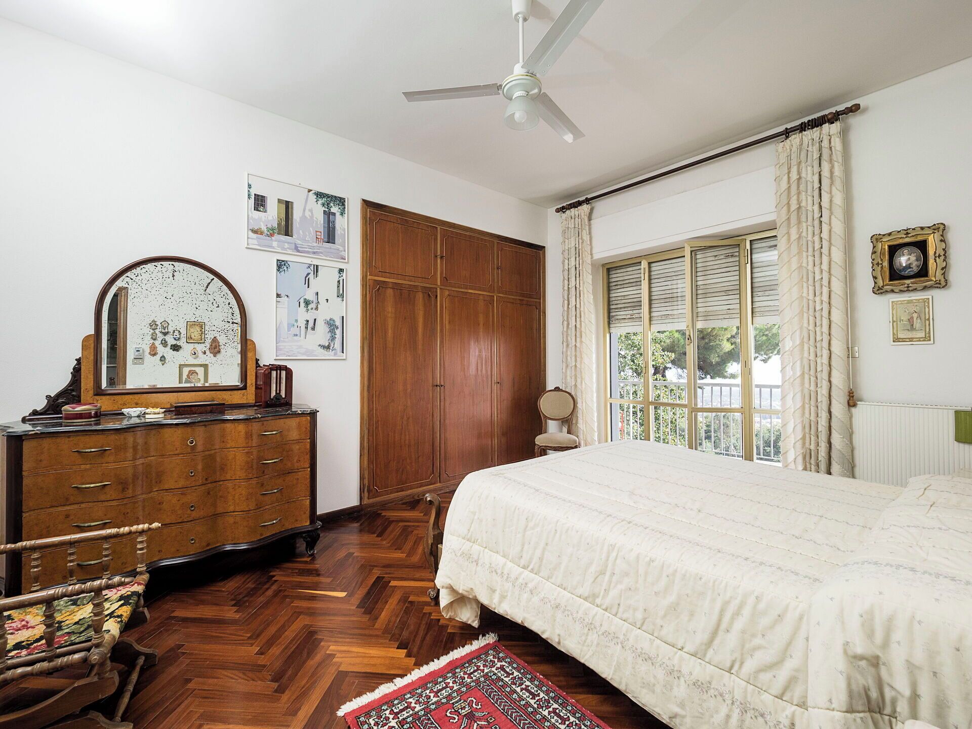 A bedroom with a bed, wooden wardrobe, dresser, chair, and a ceiling fan.