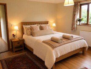 Un lit bien fait, avec une tête de lit en bois, deux lampes de chevet, un coussin à motifs floraux et une serviette enroulée posée sur le lit.