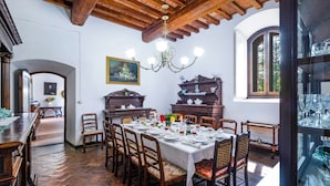 Uma sala de jantar com uma mesa comprida posta para uma refeição, cadeiras de madeira, um lustre e uma janela grande com vista.
