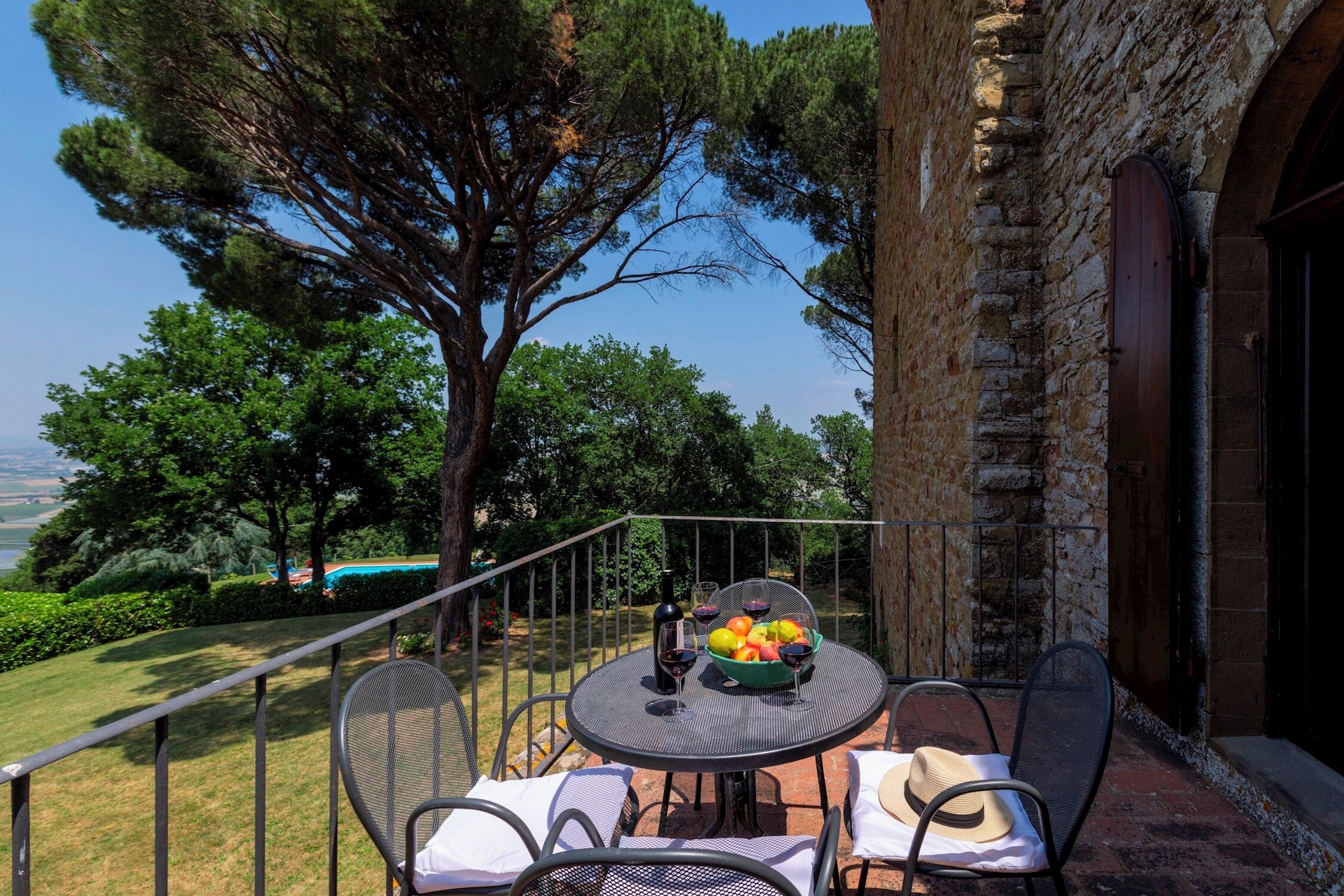 Une terrasse avec une table dressée pour deux personnes, un panier de fruits et une bouteille de vin.