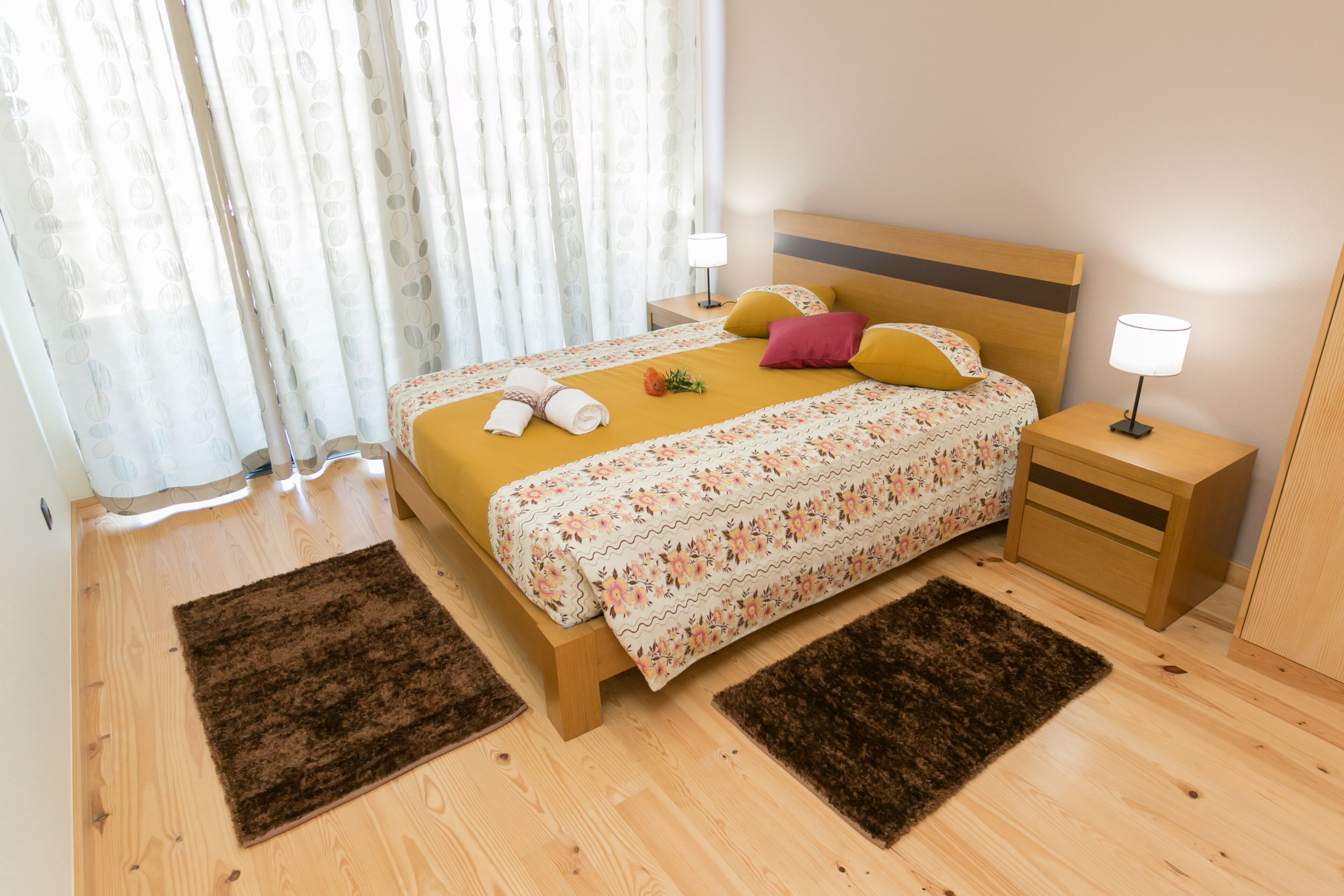 A neatly made bed with floral bedding, two bedside lamps, and a wooden headboard.
