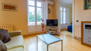 Ein Wohnzimmer mit einer Couch, einem Couchtisch, einem Fernseher und einem Fenster mit Blick auf Gebäude.