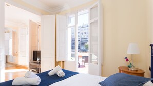 Ein Hotelzimmer mit Bett, Fernseher, Lampe und Blick auf die Stadt durch die geöffnete Tür.