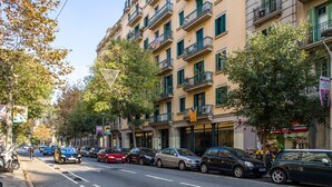Ein mehrstöckiges Gebäude mit Balkonen, parkenden Autos und Bäumen entlang der Straße.