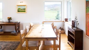 Un coin repas avec une table et des chaises en bois, un tableau accroché au mur et une vue sur l’extérieur grâce à une grande fenêtre.