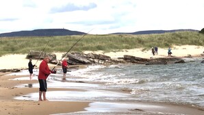 Une plage où l’on voit des gens pêcher et se promener le long du rivage.