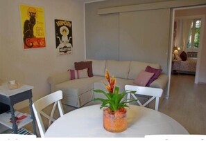 Uma sala de estar com um sofá branco, uma mesa redonda com uma planta e dois cartazes na parede.